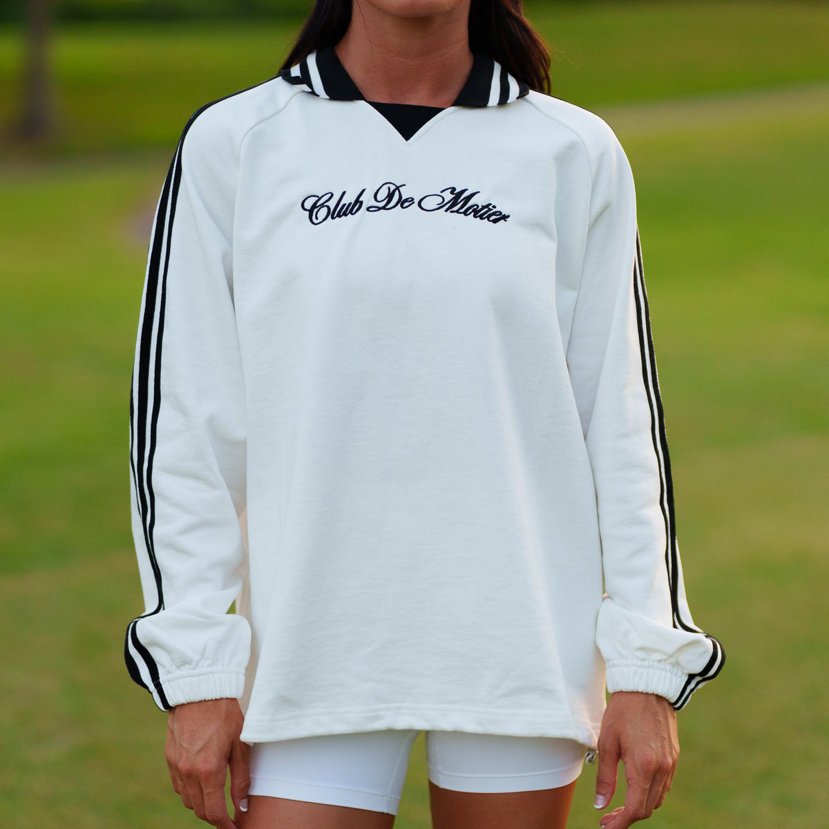White Motier Lafayette Club De Motier varsity pullover with contrasting sleeve stripes and embroidered logo, displayed on a hanger.