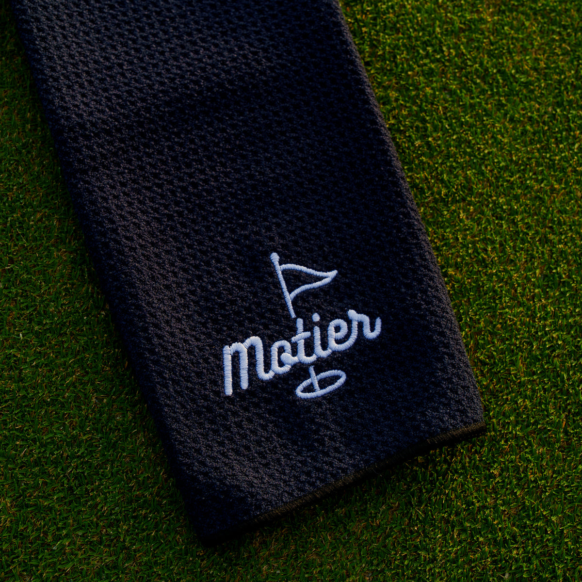 Black microfiber golf towel by Motier Lafayette with the Pin design, showing soft, absorbent fabric for cleaning golf clubs and balls.