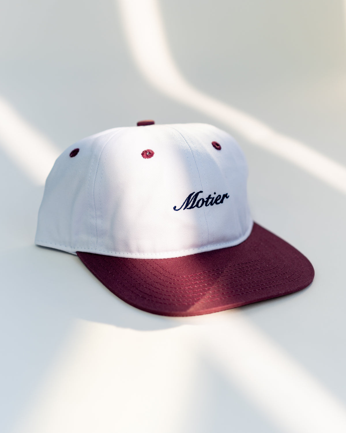 Motier Lafayette two-tone script strapback hat in maroon, white, and navy with adjustable strap and embroidered logo.