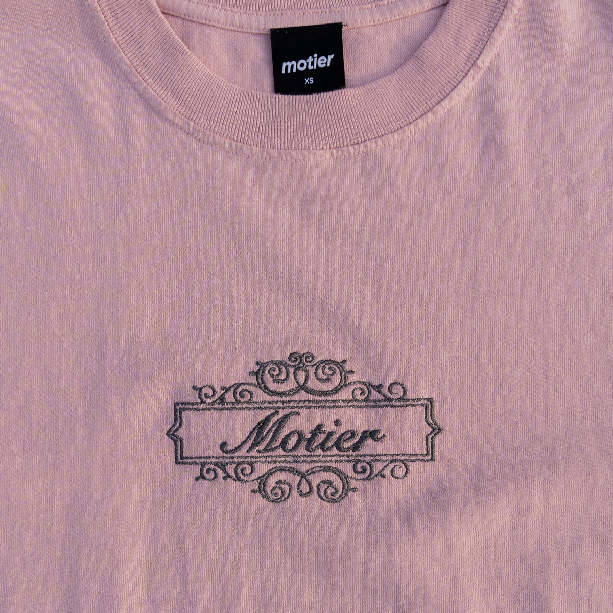 Pale mauve Motier Lafayette Royale Crest Embroidery Premium Luxe Tee, close-up of embroidered crest on soft cotton fabric.