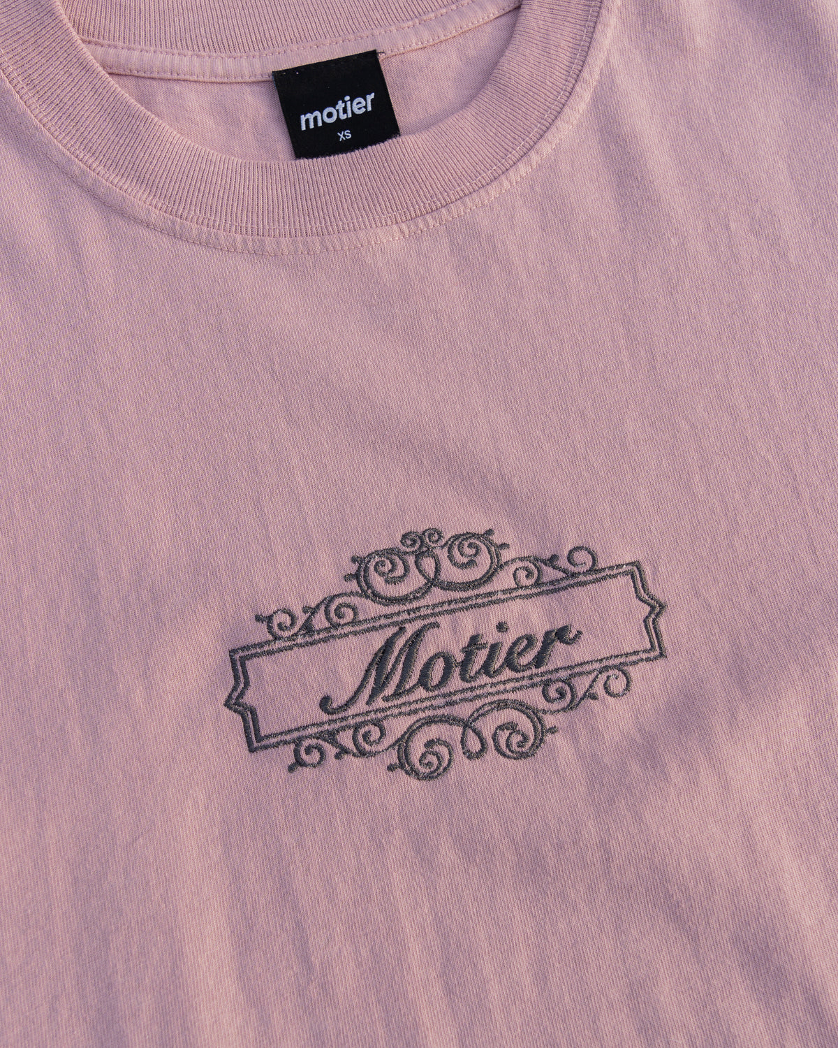 Motier Lafayette The Royale Crest Embroidery Luxe Tee in Pale Mauve, showing a close-up of detailed crest embroidery on the premium cotton tee.