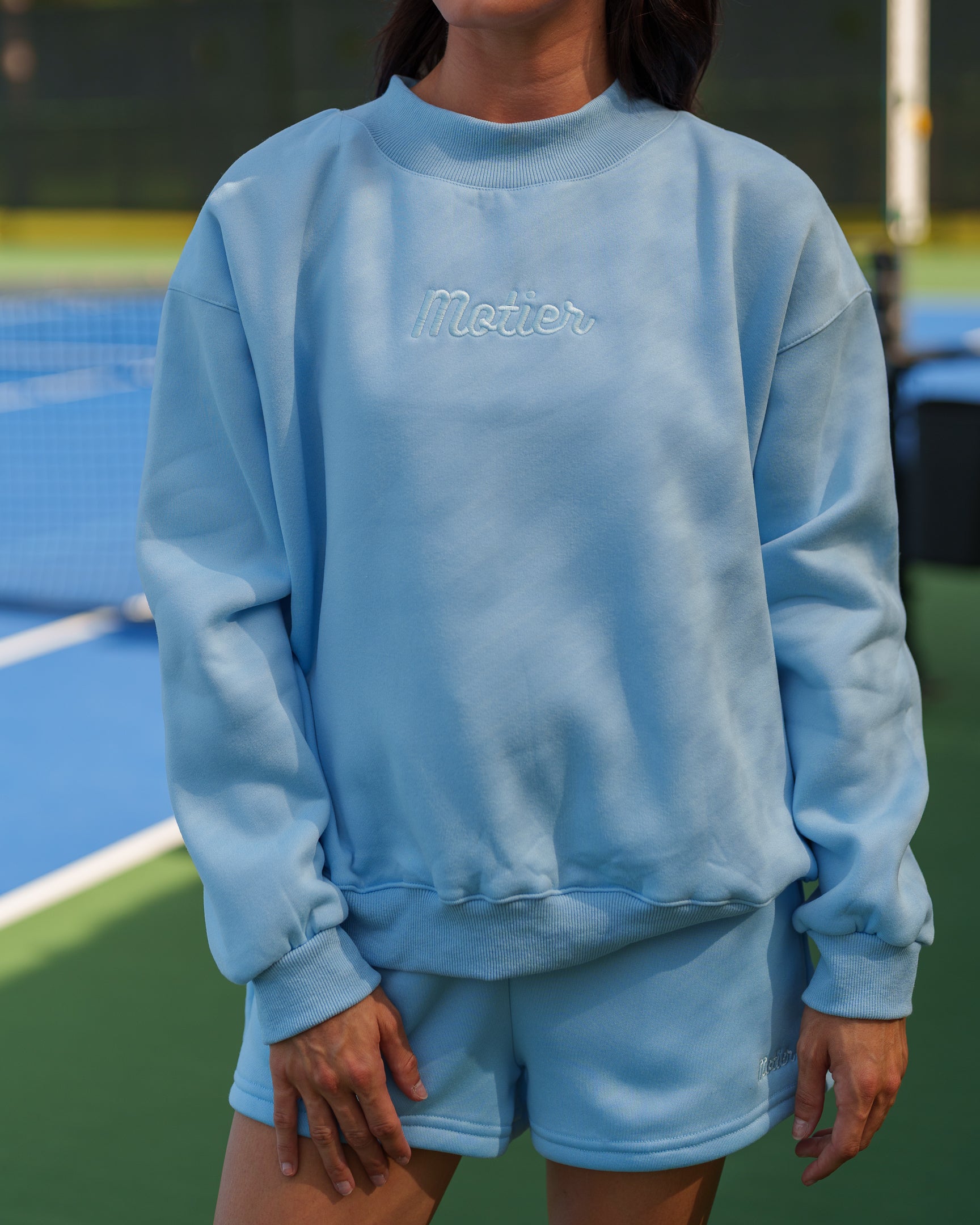 Sky blue The Pin Script Mock Neck sweater by motierlafayette, featuring a soft knit fabric and a stylish mock neck design.