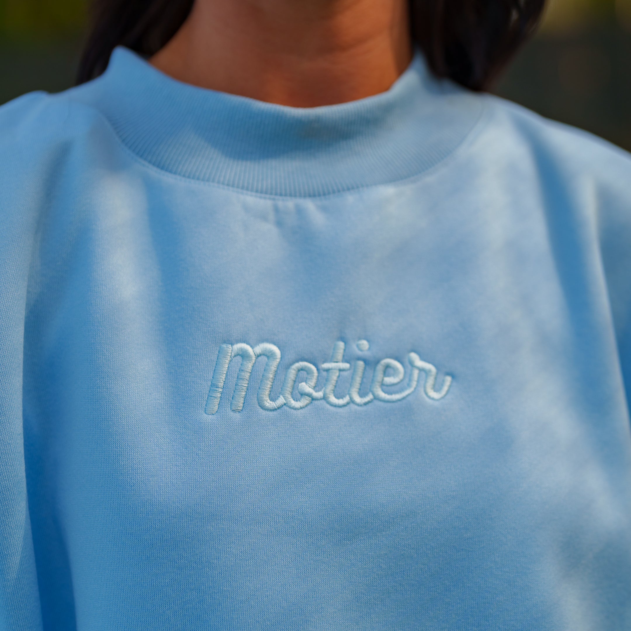 Sky blue motierlafayette Pin Script Mock Neck sweater displayed on a hanger, showing its soft fabric and stylish neckline.